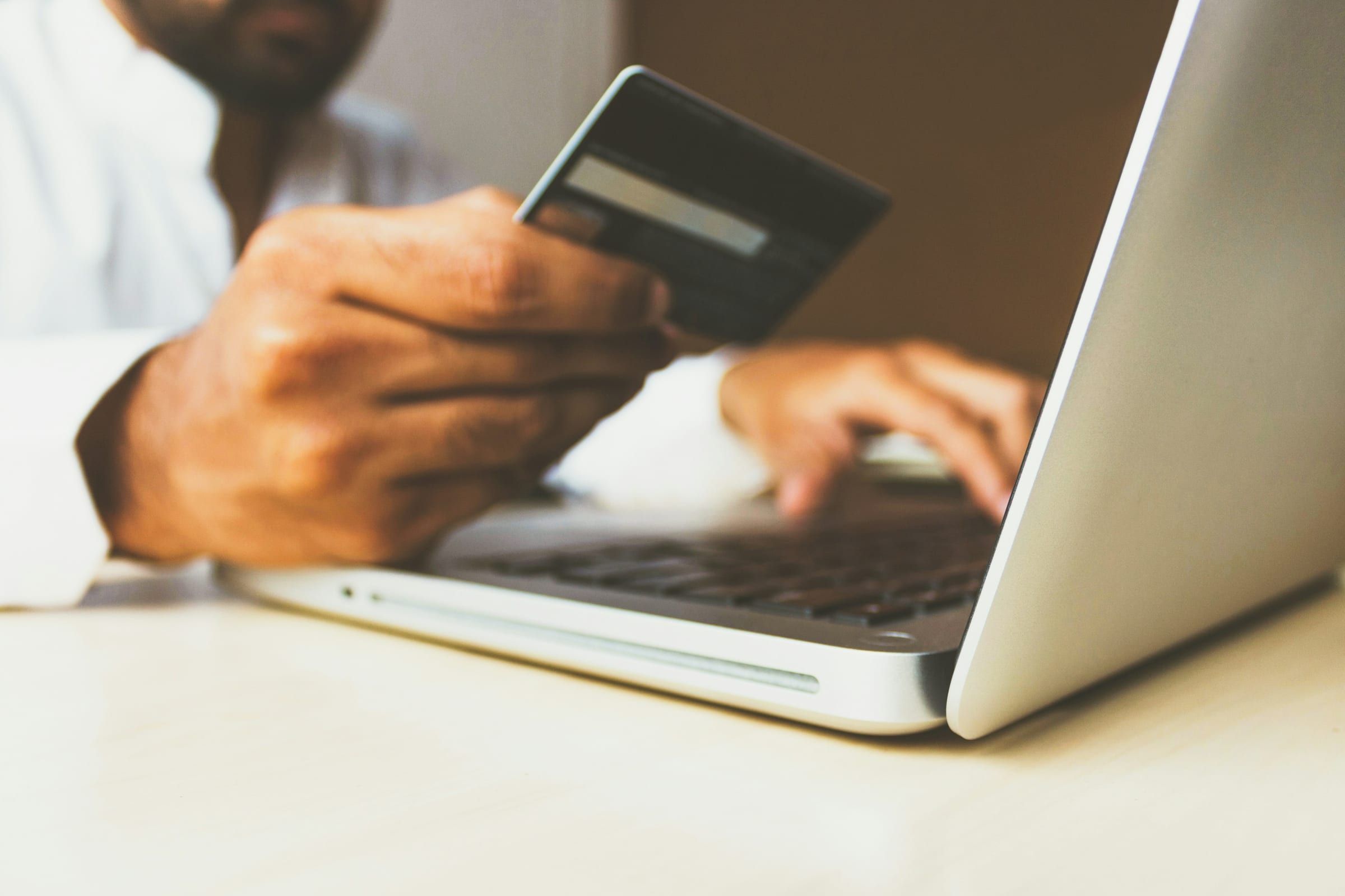 Close-up of a hand holding a payment card while the other hand types on a silver laptop
