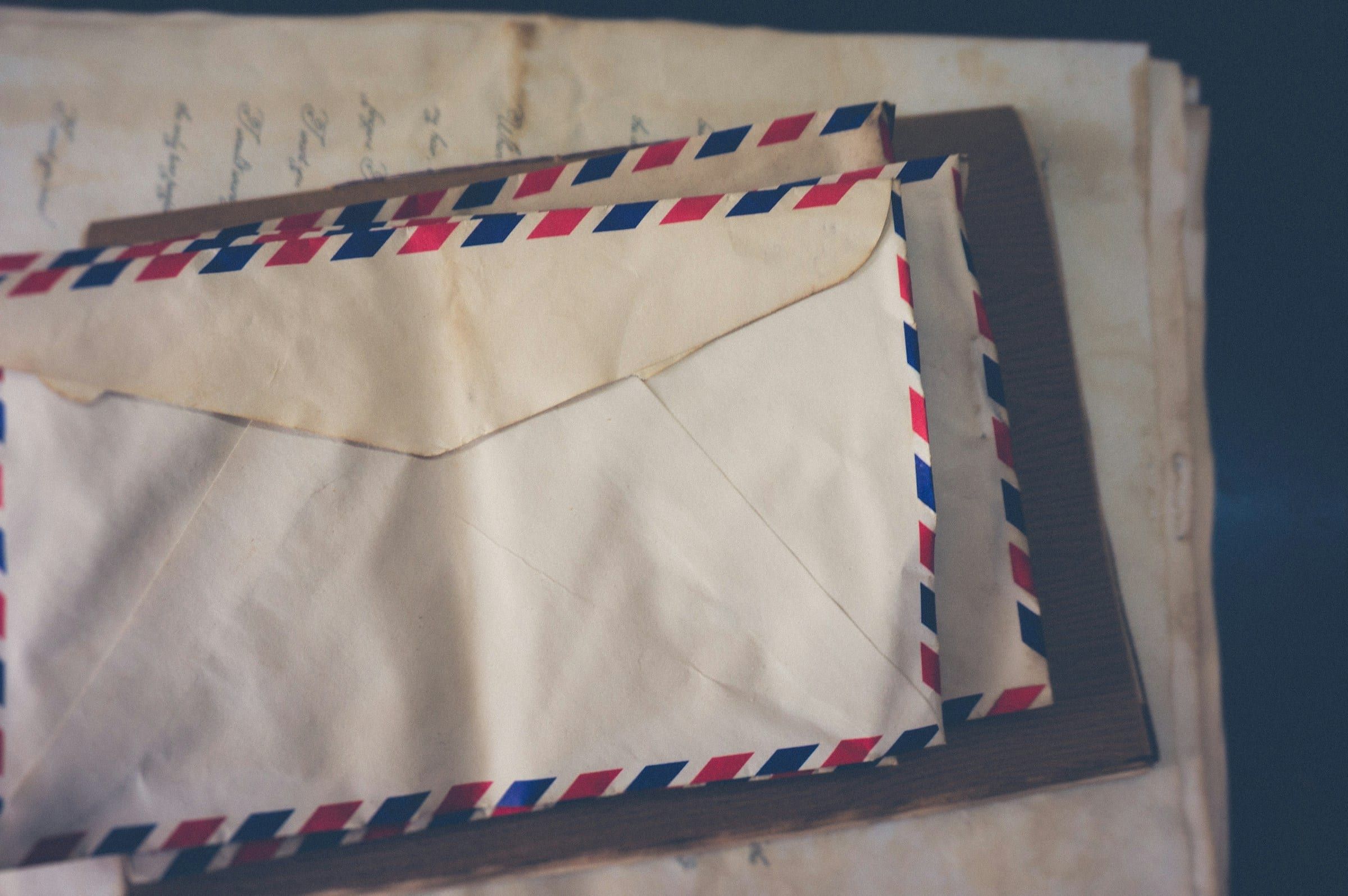 A stack of airmail envelopes with red and blue striped edges on a worn wooden surface