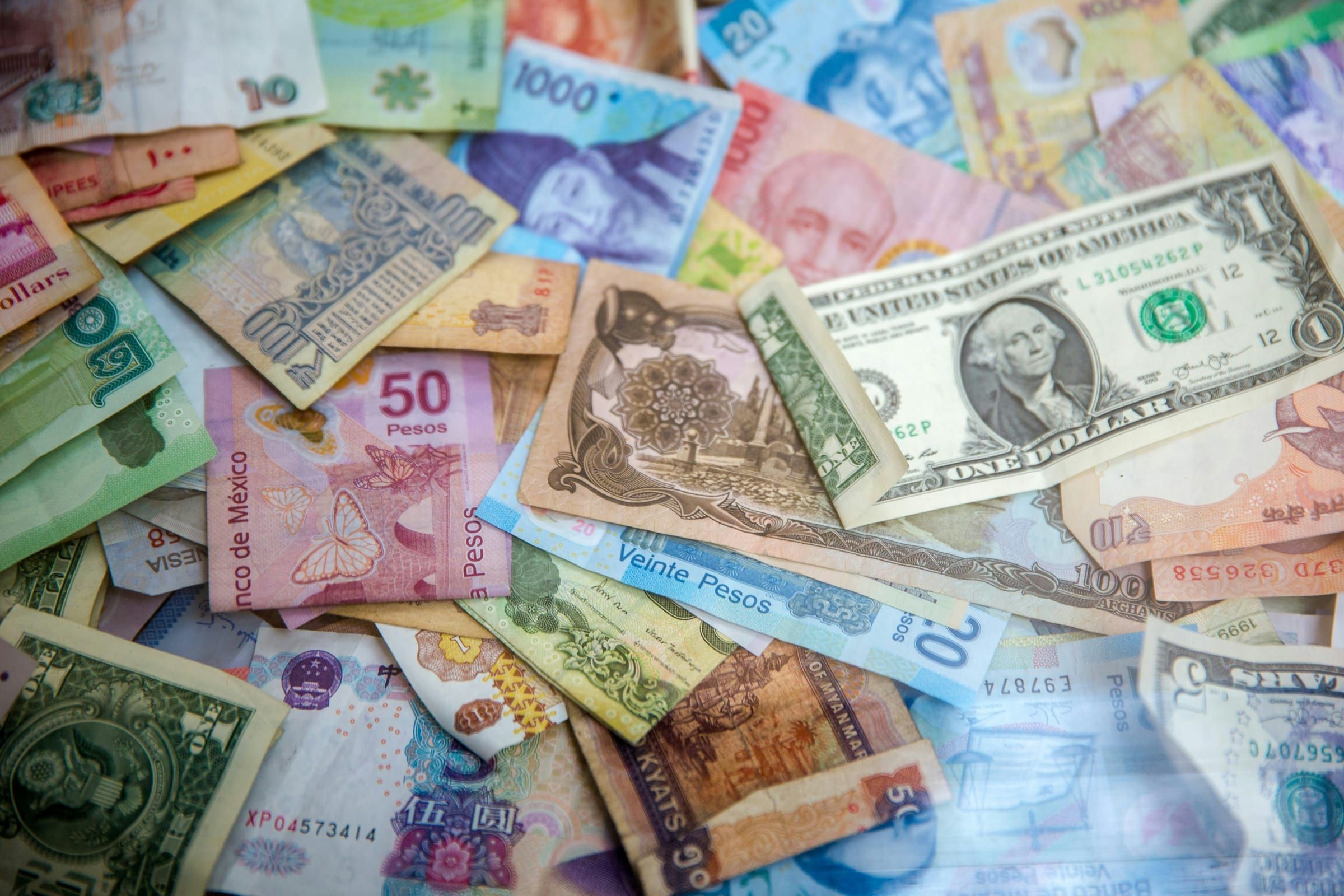 Um monte de notas de vários países, incluindo dólares americanos e pesos mexicanos, espalhadas sobre uma superfície plana