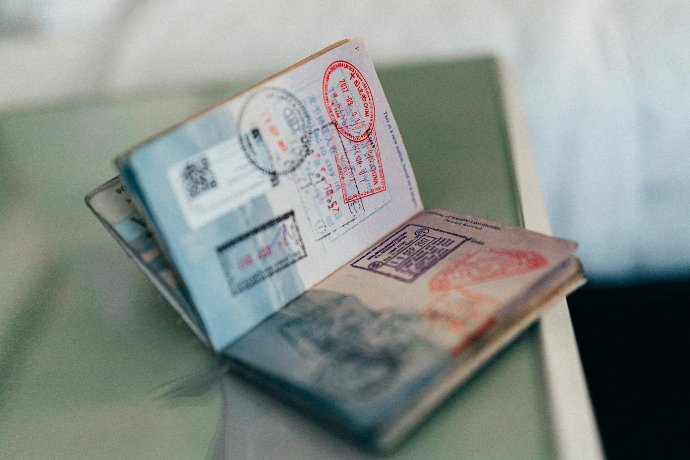 An open passport with colourful entry stamps resting on a pale green surface