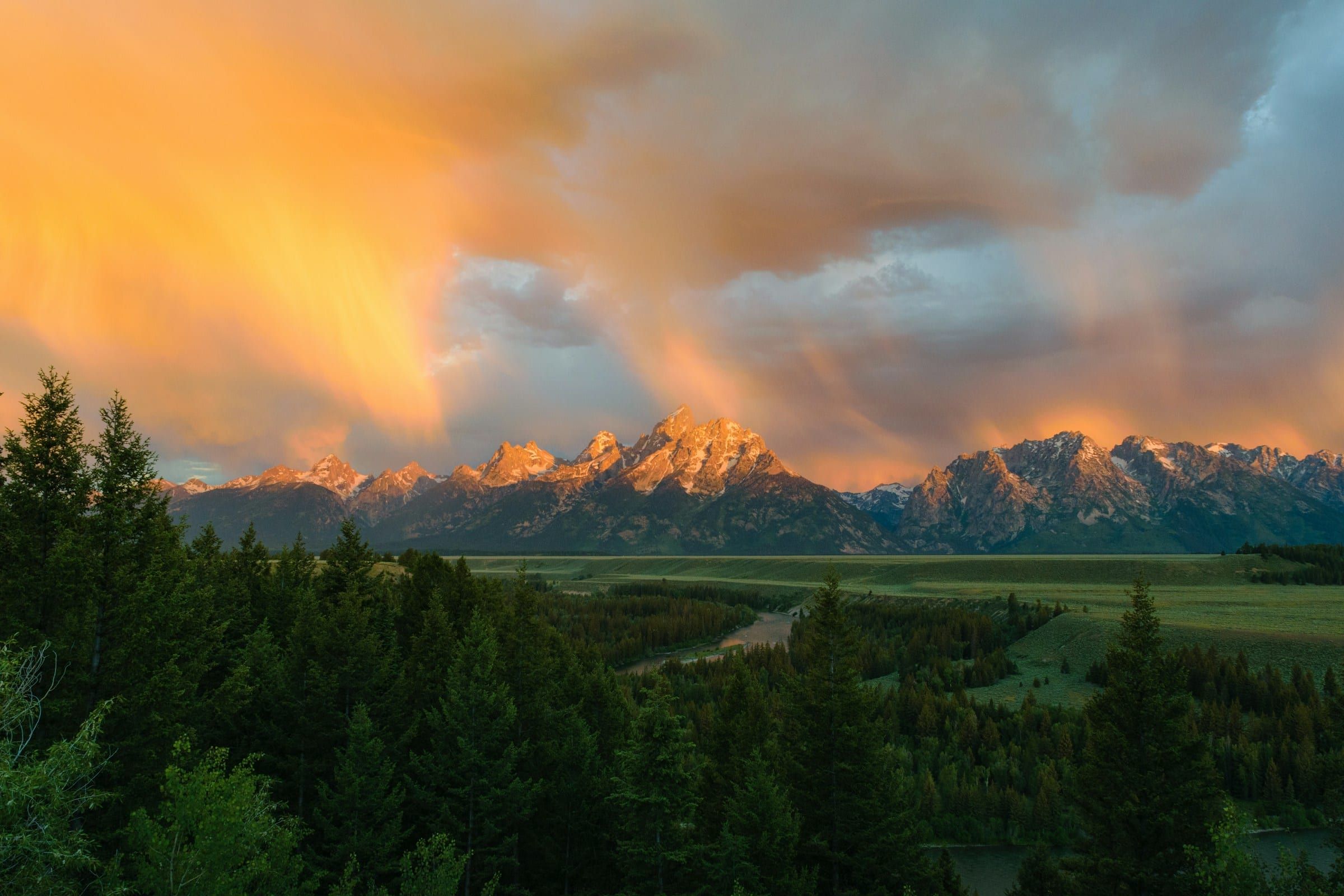 Sunset clouds glow orange over the Teton Range and a forested valley in Wyoming