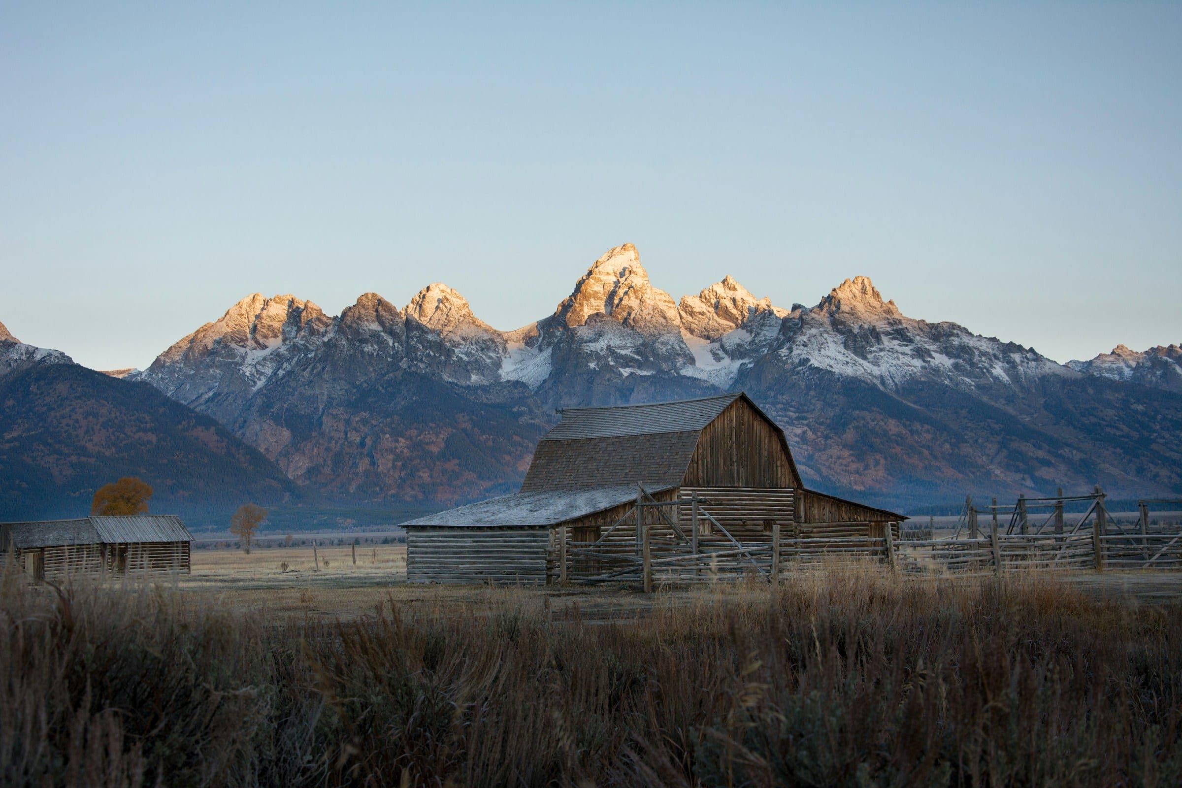A weathered wooden barn below the snowy peaks of the Teton Range in Wyoming at first light