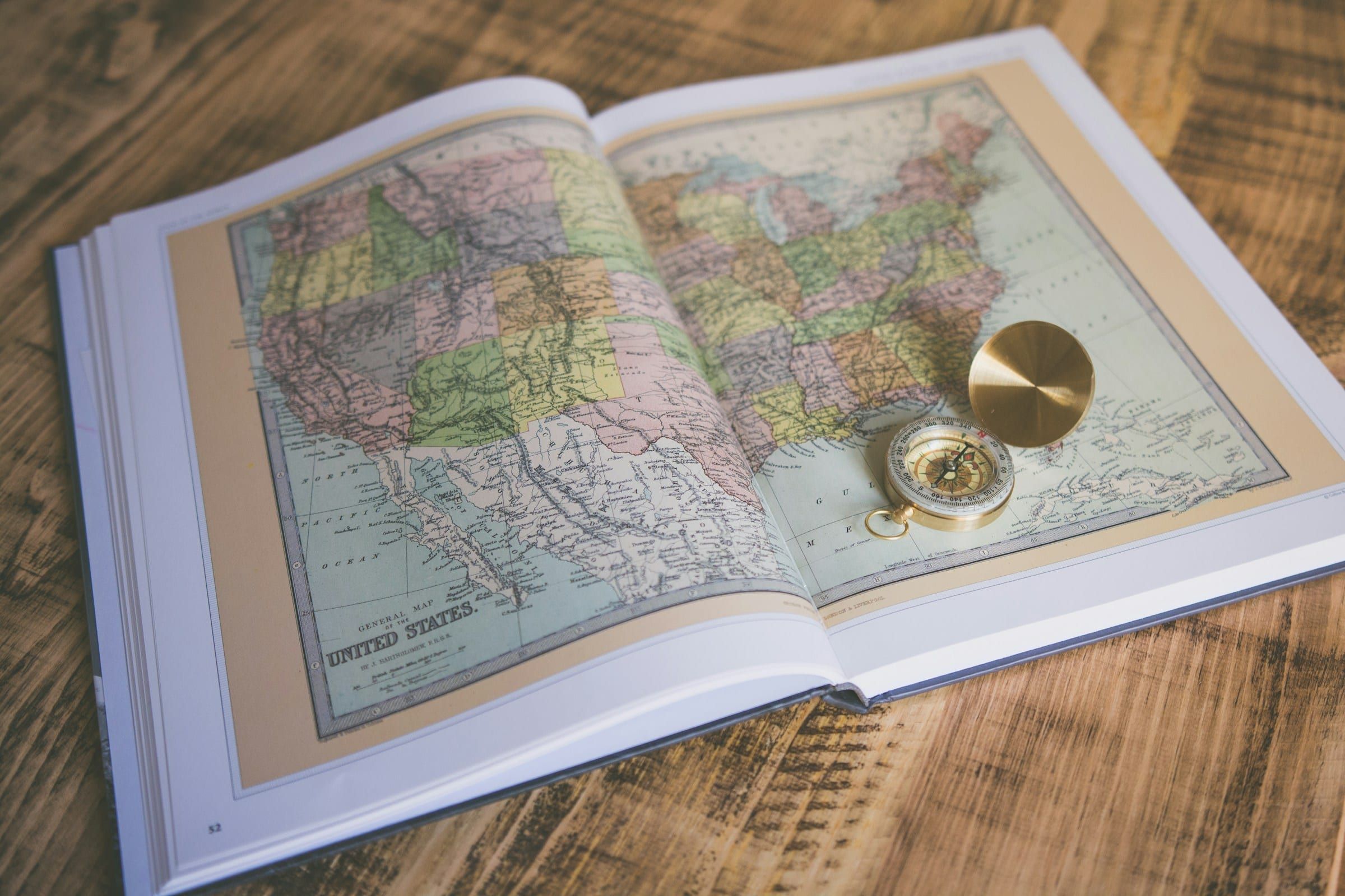 A brass compass on an open atlas showing a map of the United States on a wooden table