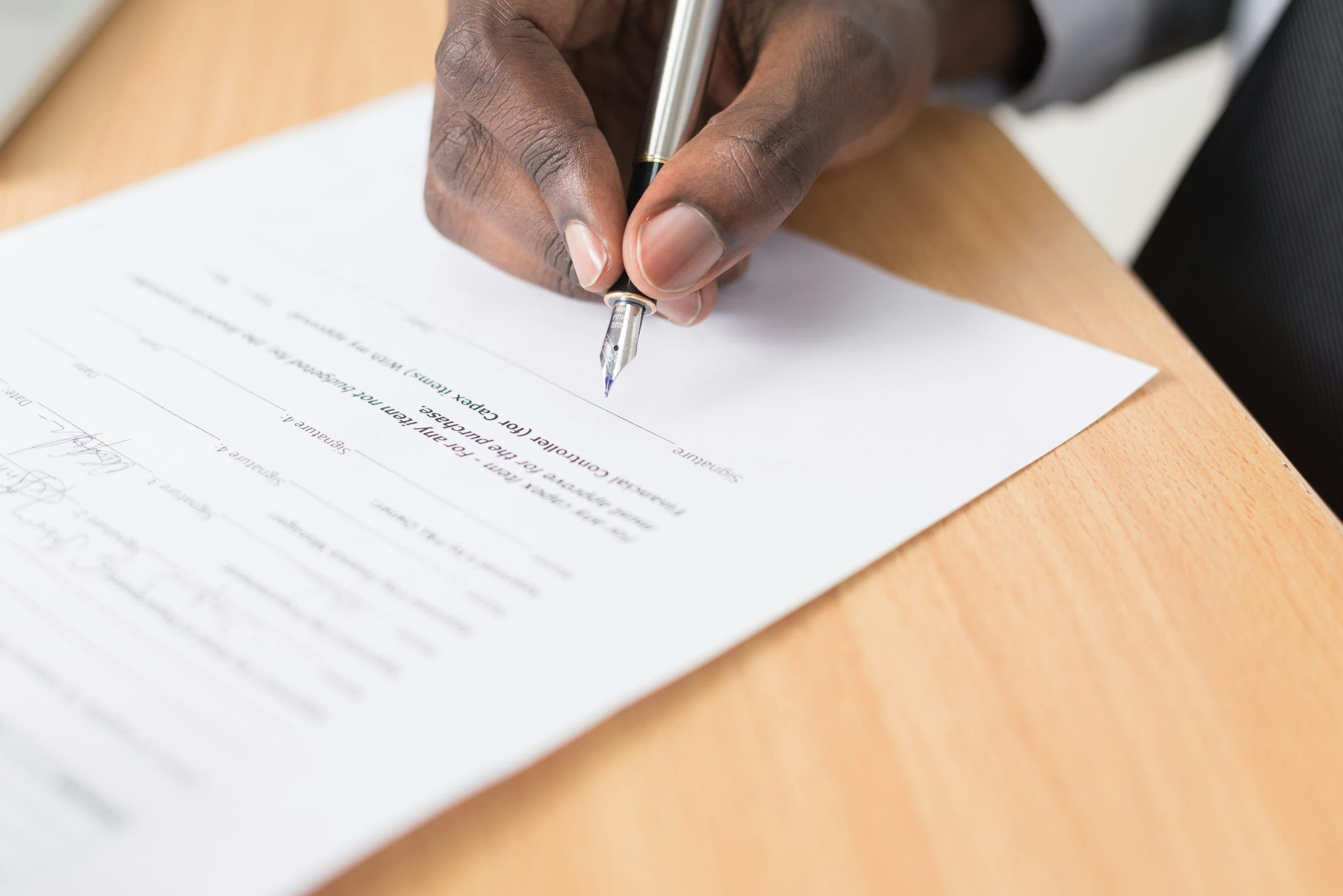 Close-up of a hand signing a printed form with a fountain pen on a light wooden desk