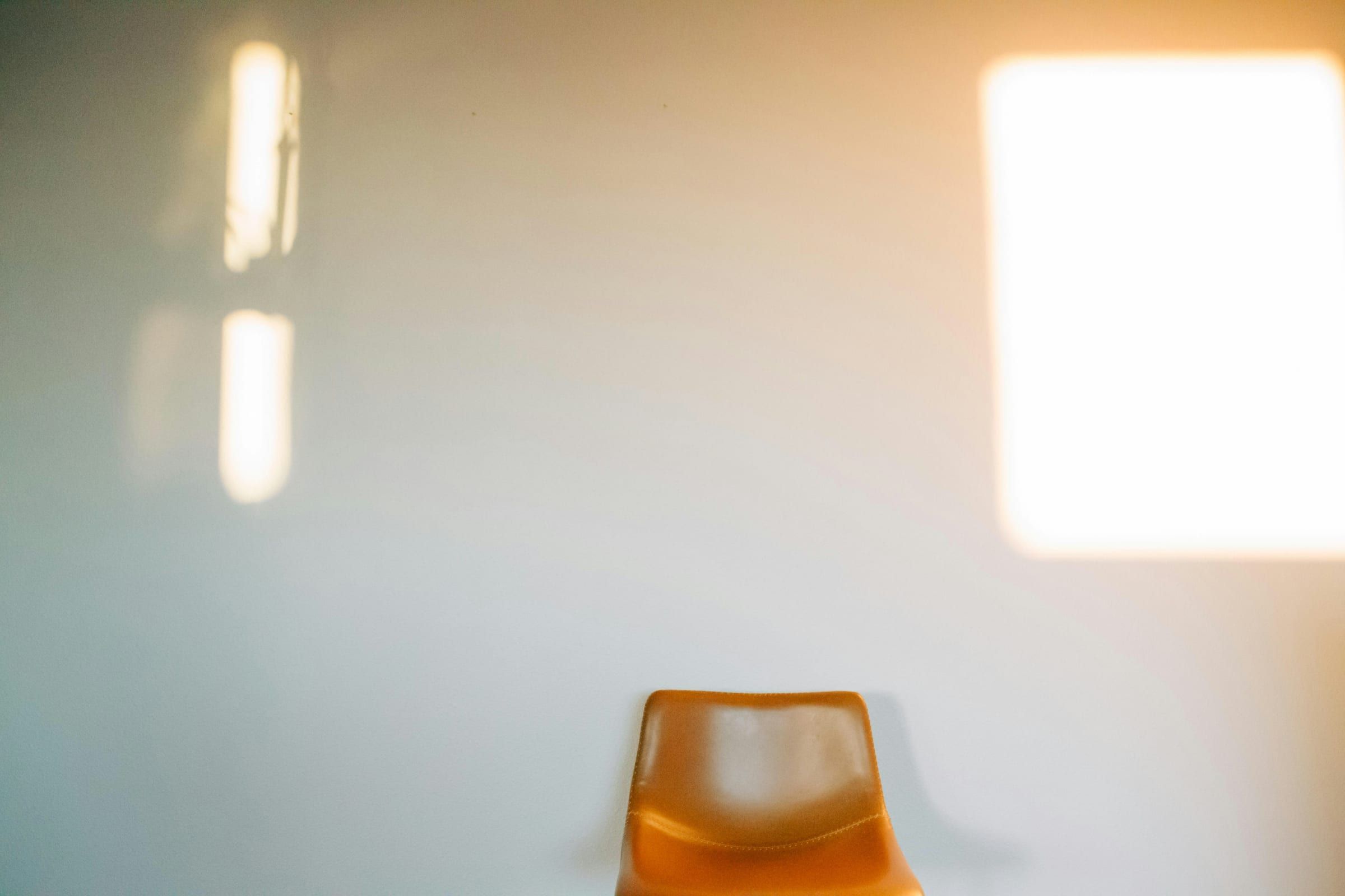 An orange stool in a pale room, with warm window light falling on the plain wall behind it